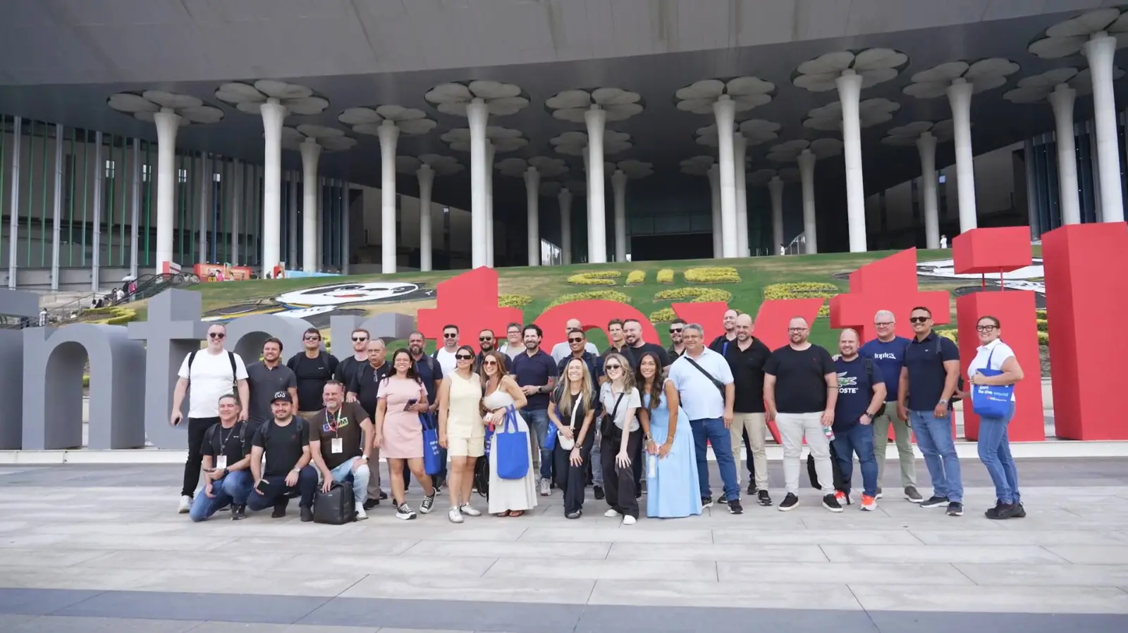 Equipe da City Comex e parceiros na entrada do NECC em Xangai durante a Intertextile Shanghai 2025, posando em frente ao letreiro do evento.